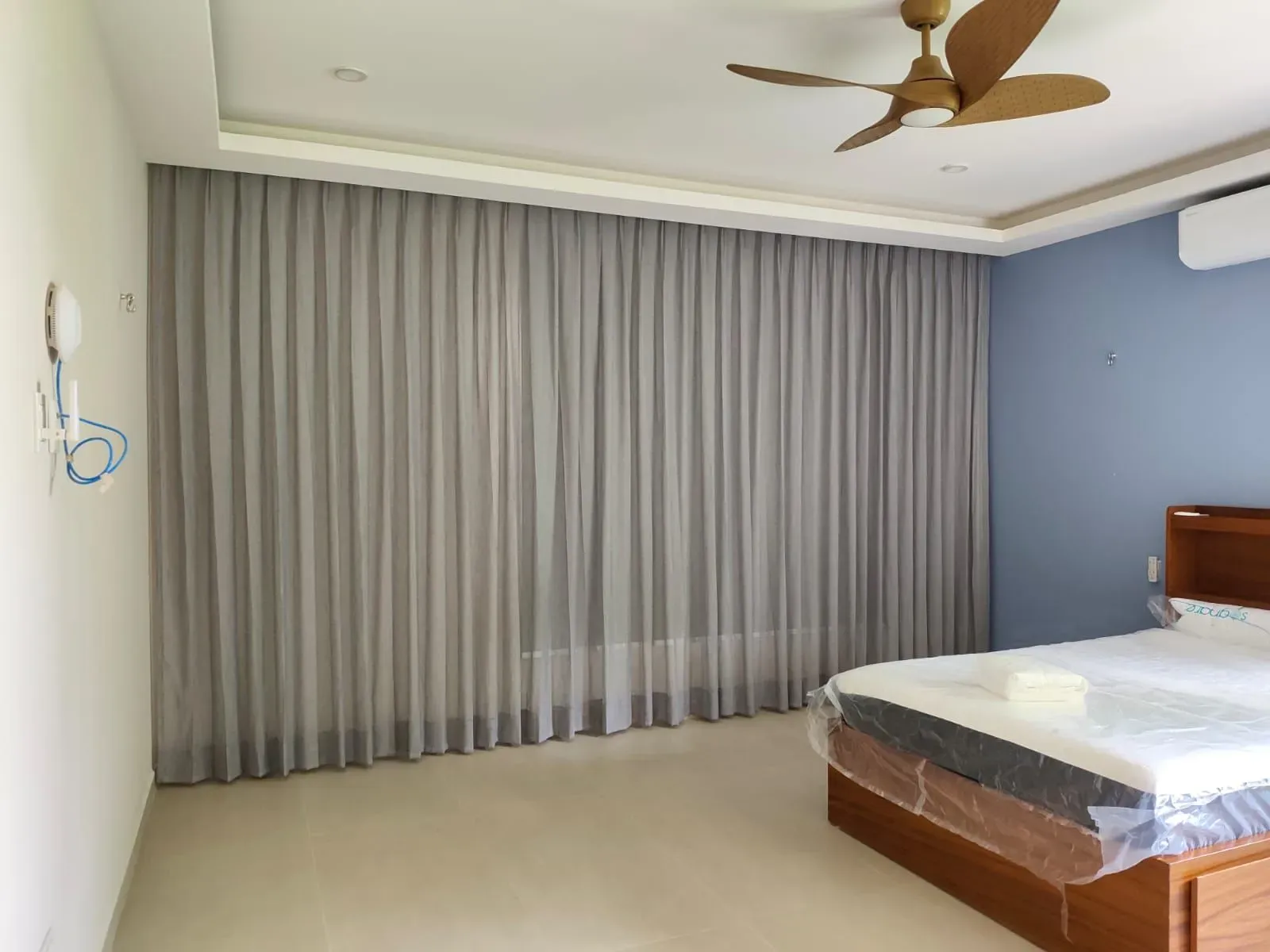 Cortina gris de piso a techo en una recámara con cama y ventilador de techo